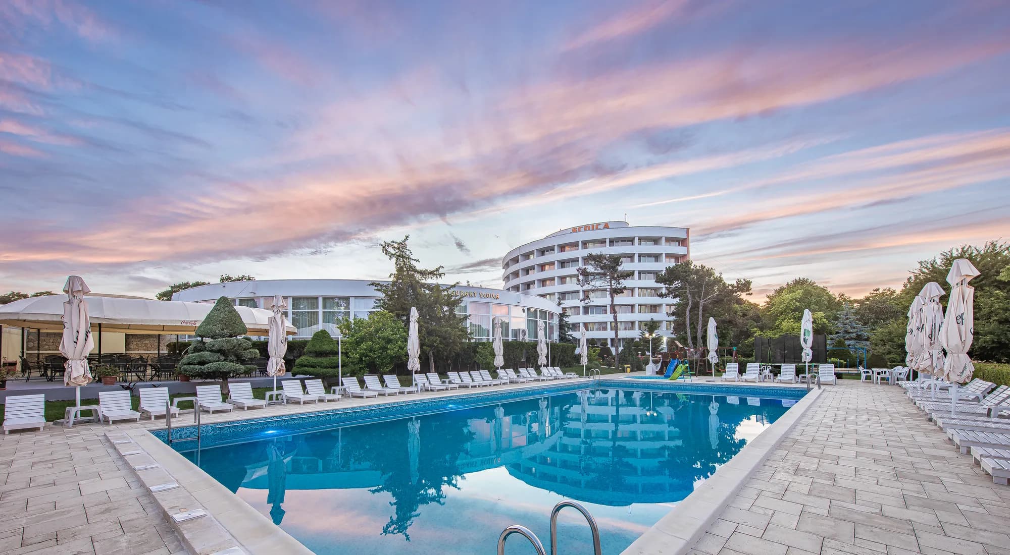 Piscina principală a hotelului la apus, sub un cer roz de vară