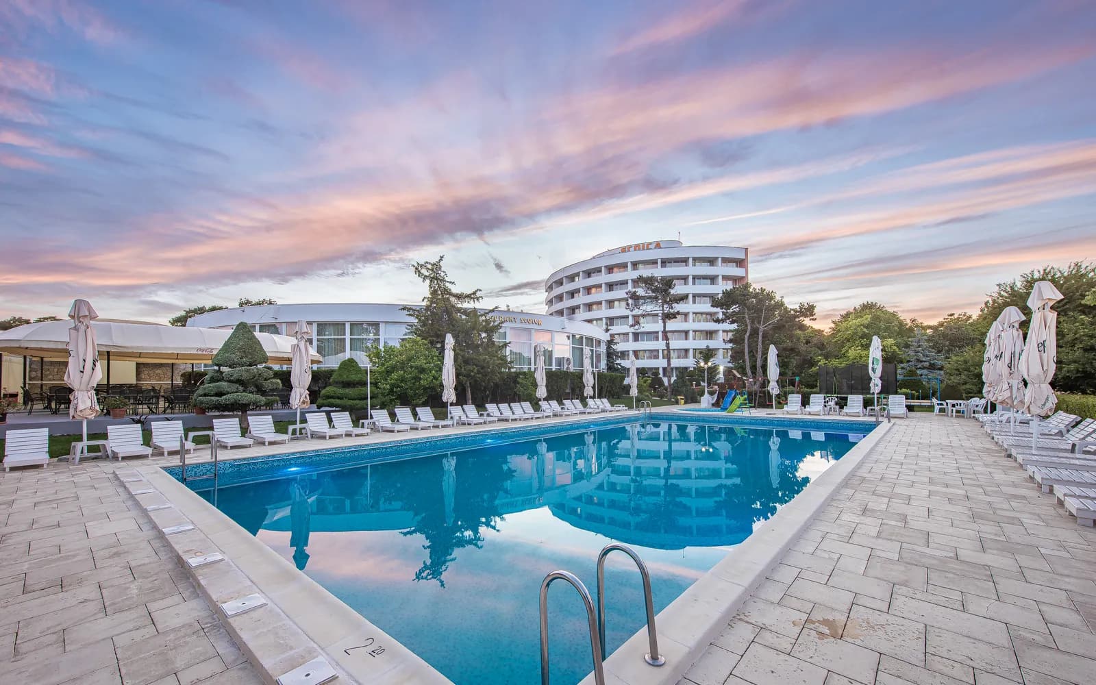 Piscina principală a hotelului la apus, sub un cer roz de vară